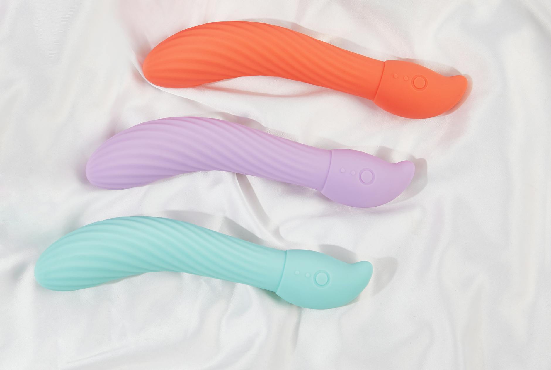 Drie gekleurde clitorale vibrators op wit weefsel, die hun gladde textuur benadrukken