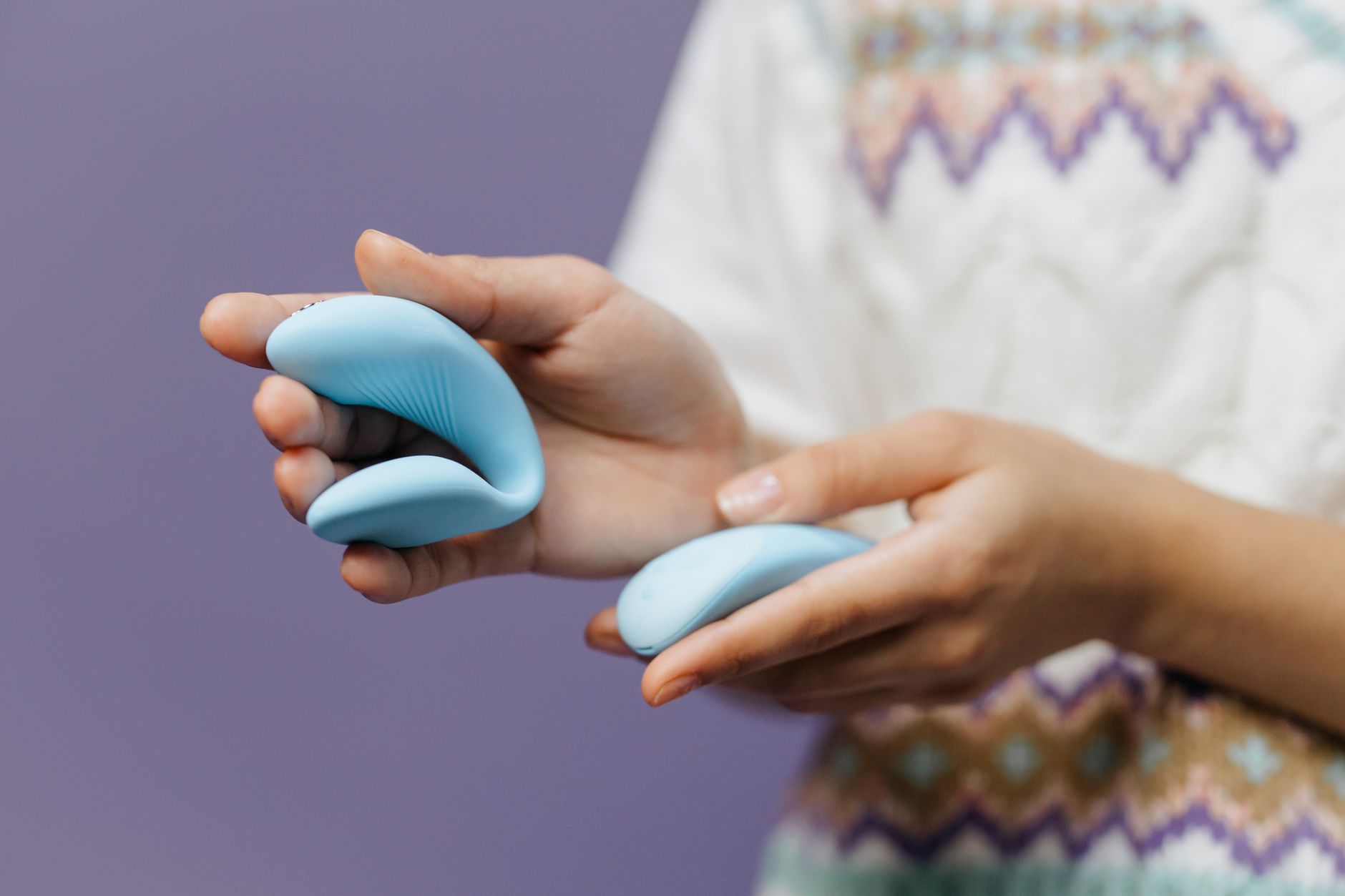Handen houden een gladde blauwe vibrator vast tegen een paarse achtergrond.