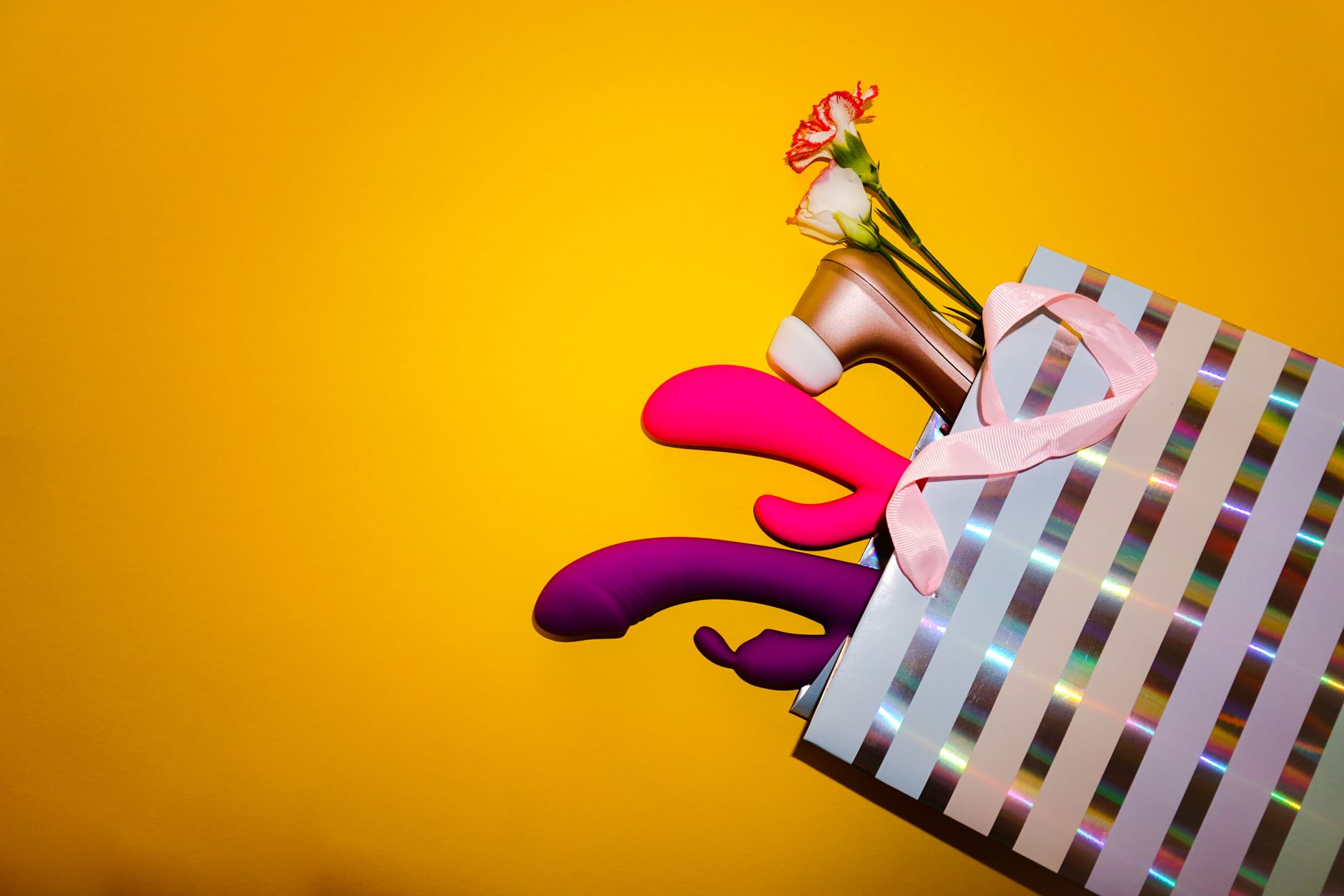 Kleurrijke vibrators met bloemen in een holografische geschenkzak op gele achtergrond